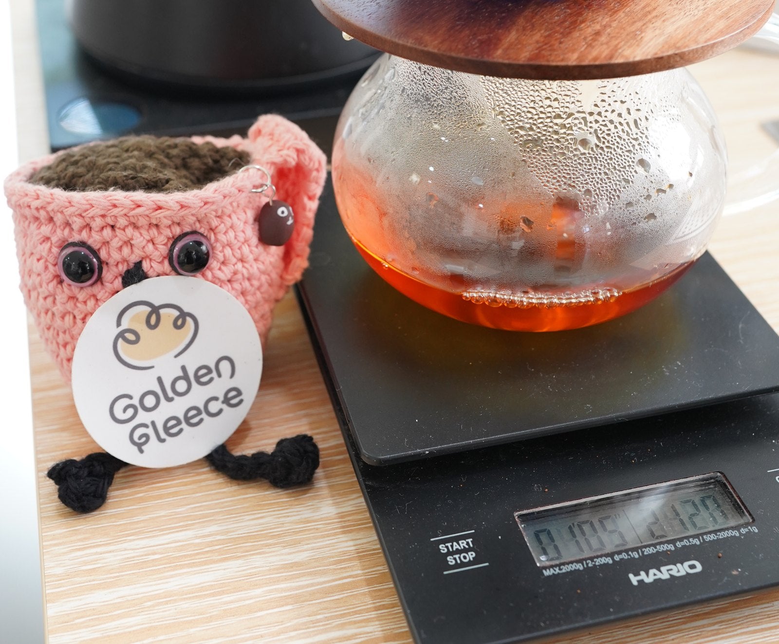 A knitted Golden Fleece mascot mug beside a glass carafe of freshly brewed coffee